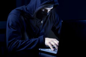 hacker in black with mask using laptop computer